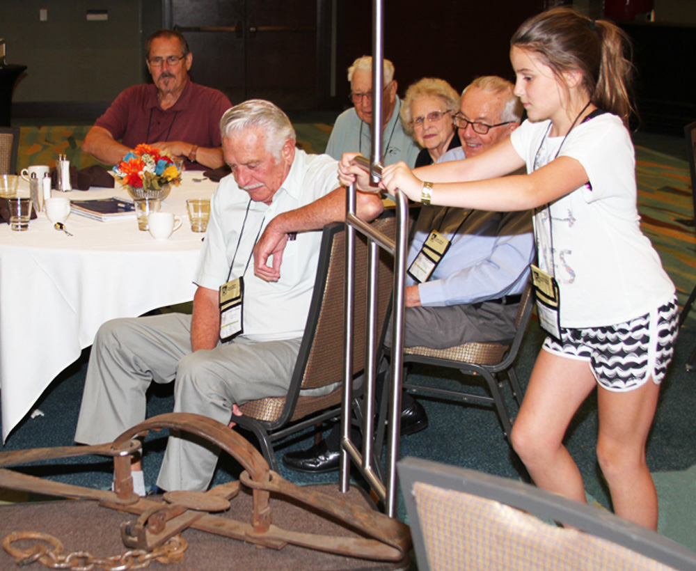 Maggie Boley at about 10 years old pushing a cart with Oxen harness at an OCTA conference with 5 members sitting around a table watching.